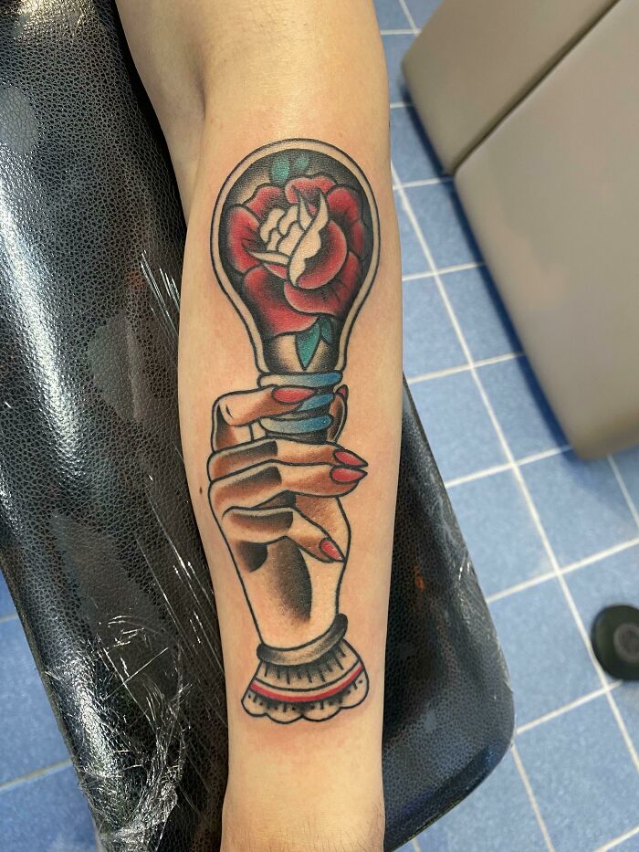 American traditional tattoo of a hand holding a rose-adorned light bulb on forearm.