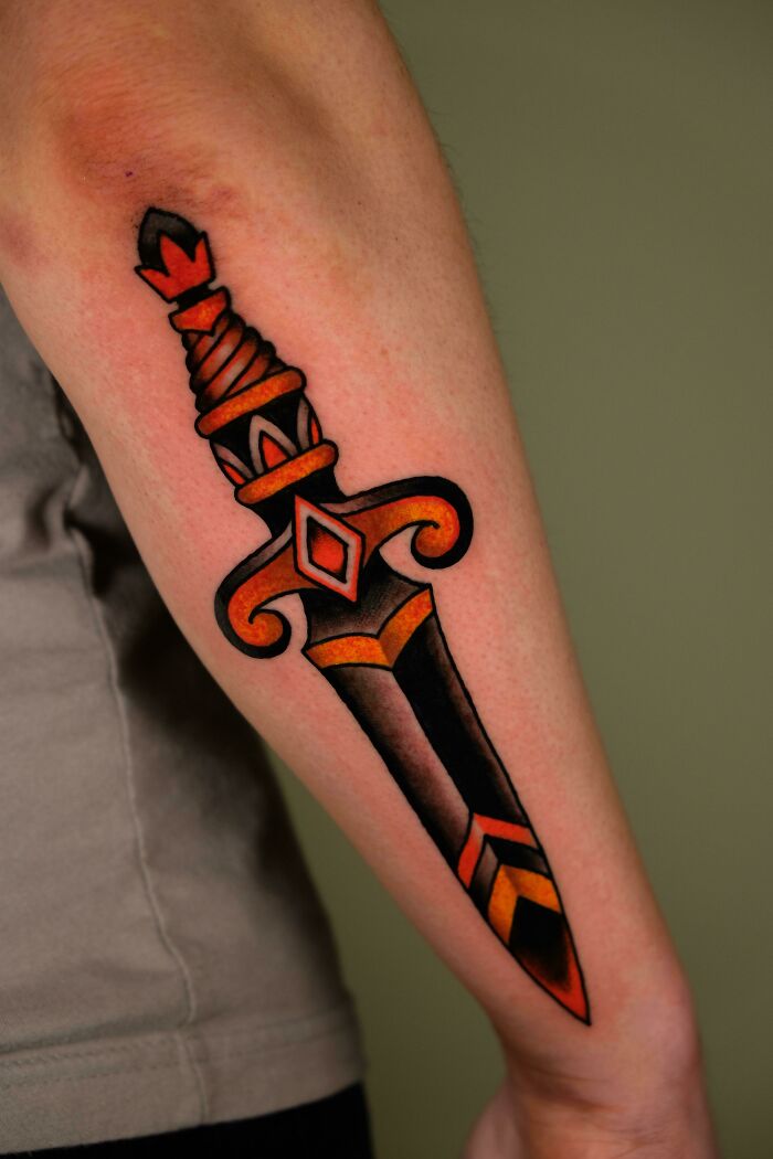 American traditional dagger tattoo with bold black and red colors on forearm for a timeless look.