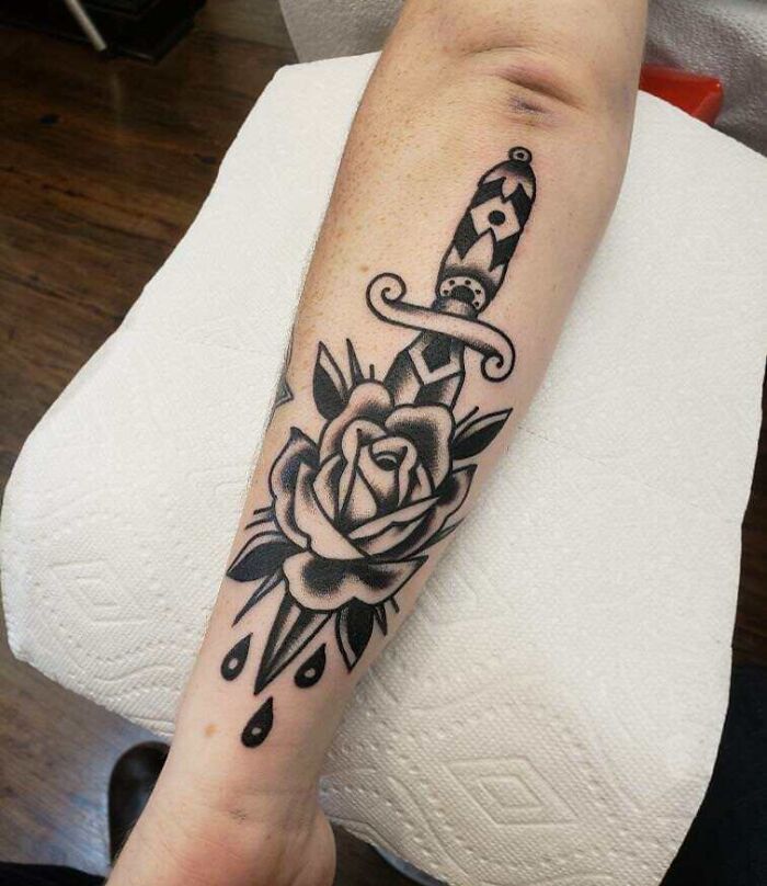 Arm with an American traditional tattoo showcasing a dagger through a rose, symbolizing timeless art.
