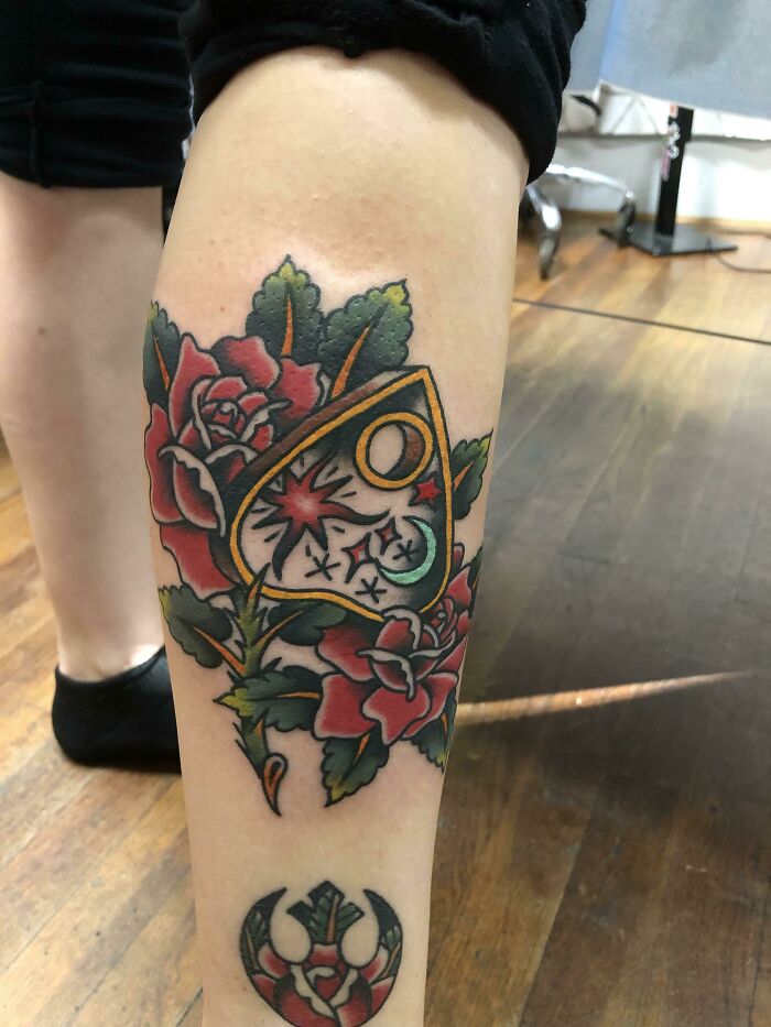 American traditional tattoo featuring red roses and a symbolic design on a leg.