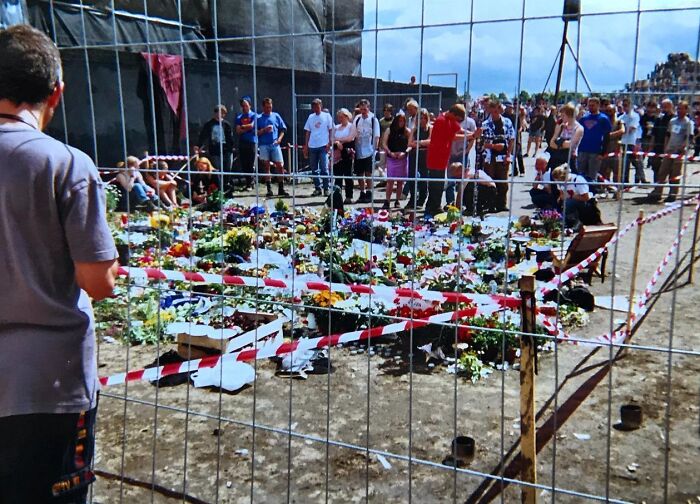 A fenced area with flowers and people around in the Roskilde Festival, 2000
