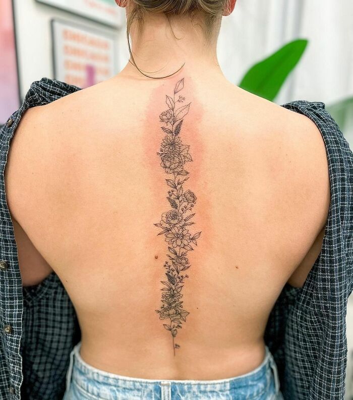 Floral spine tattoo design on a woman's back, showcasing intricate flower details and artistic placement.