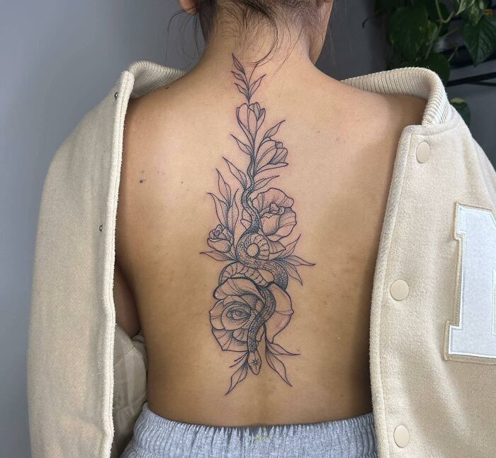 Snake and flowers tattoo on woman’s spine