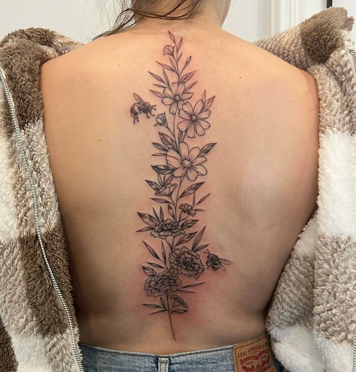 Floral spine tattoo with bees on person's back, showcasing intricate design and artistry.
