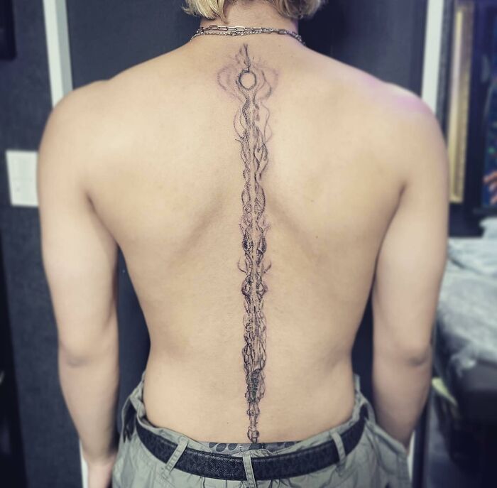 Intricate spine tattoo design on a person's back, showcasing detailed linework and artistry.