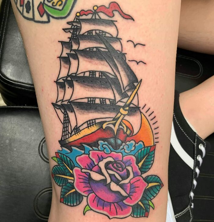 American traditional tattoo of a sailing ship with a colorful rose design on skin.