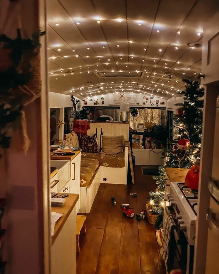 Cozy tiny house interior with string lights, decorated for the holidays, featuring a small kitchen and seating area.