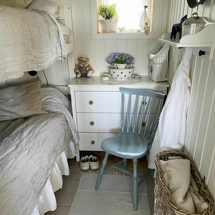 Cozy tiny house interior with bunk bed, dresser, and pastel blue chair, showcasing charming and efficient design.