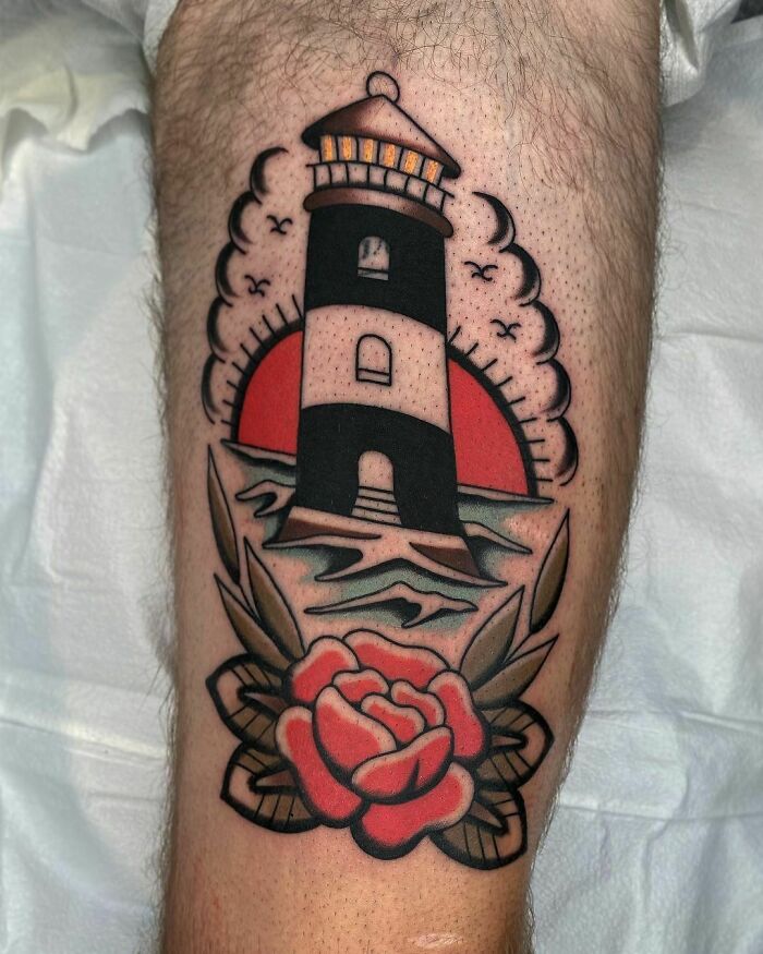 American traditional tattoo of a lighthouse with a red rose and ocean waves, showcasing timeless design.