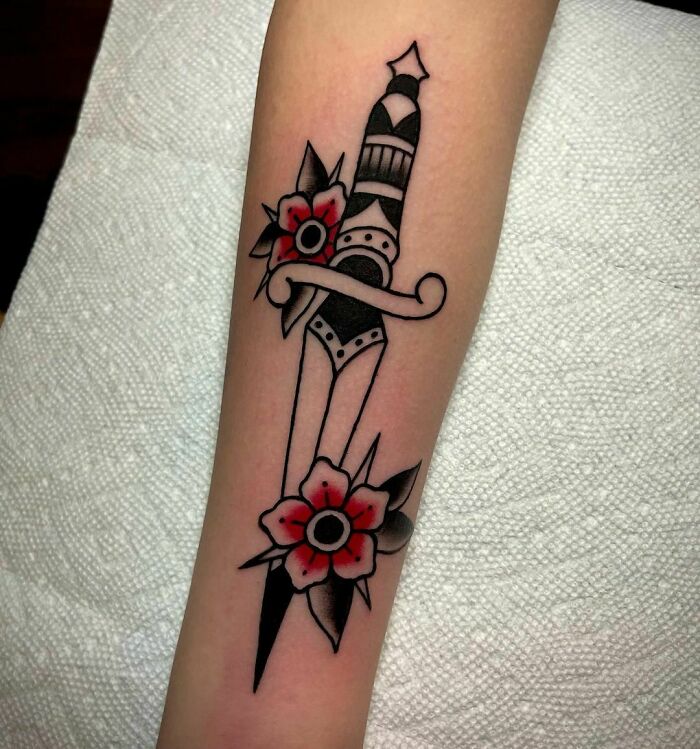 American traditional tattoo of a dagger with red flowers on an arm.