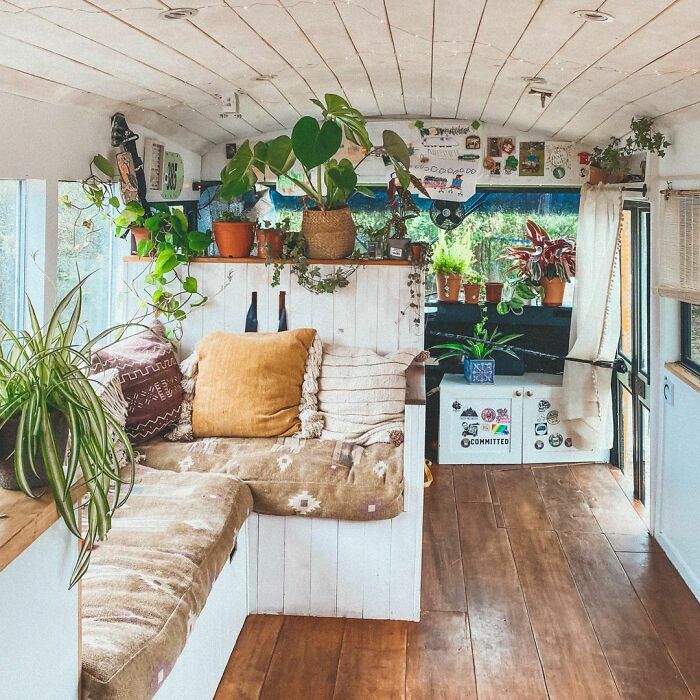 Cozy white tiny house van interior filled with plants, warm cushions, and natural wood flooring creating a peaceful living space.