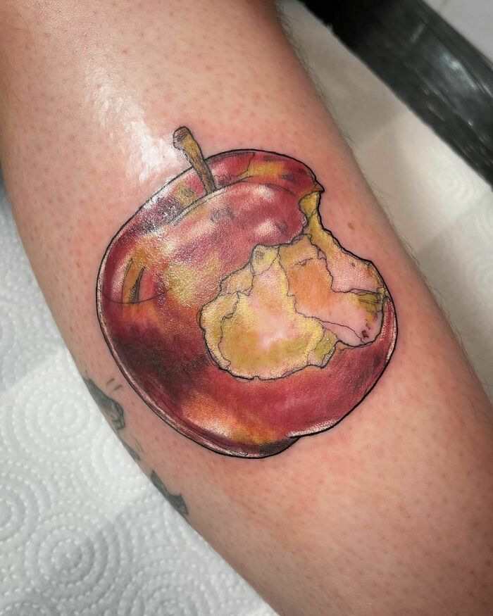Watercolor tattoo of a bitten apple on skin, showcasing creative food-themed ink-spiration.