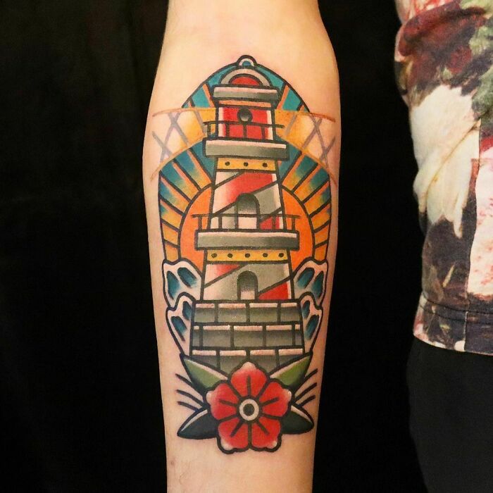 American traditional tattoo of a lighthouse and red flower on forearm, featuring bold colors and classic design elements.