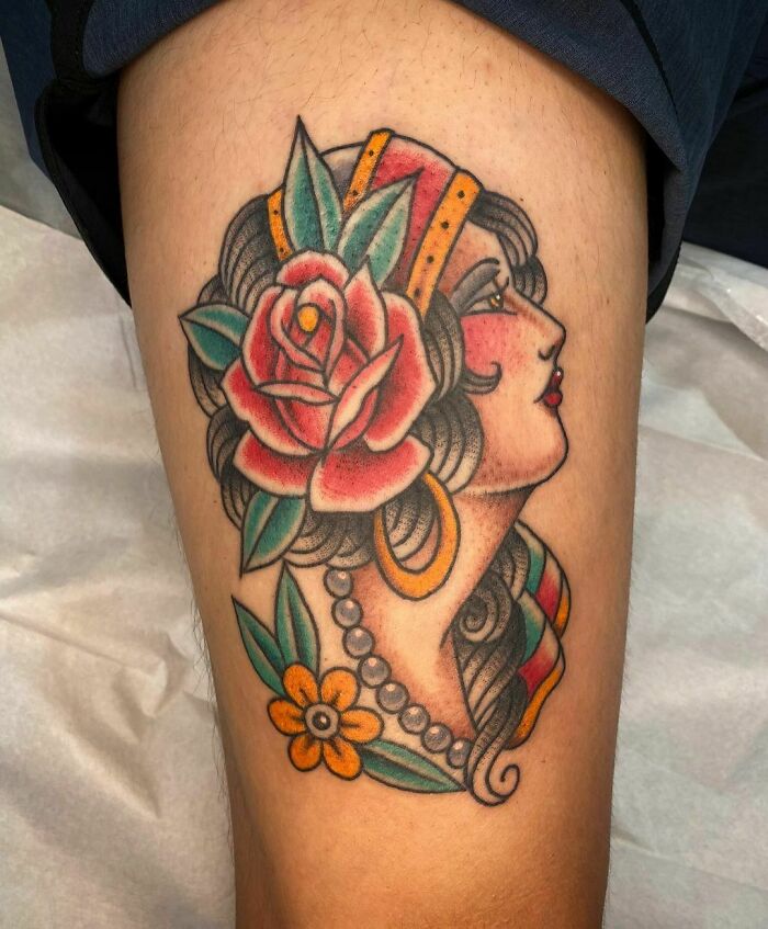Colorful American traditional tattoo featuring a woman with a rose and flower detail on her arm.