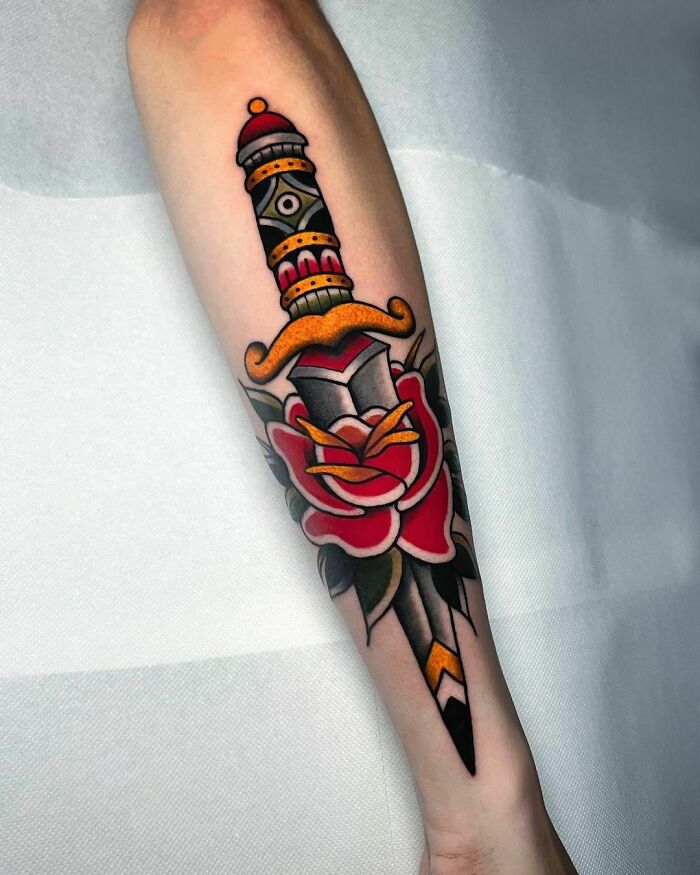 American traditional tattoo of a dagger through a rose, featuring bold colors and classic design on forearm.