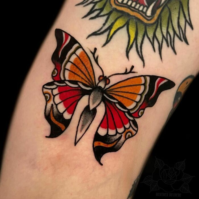 American traditional tattoo of a colorful butterfly on arm, showcasing bold red and orange hues for a timeless look.
