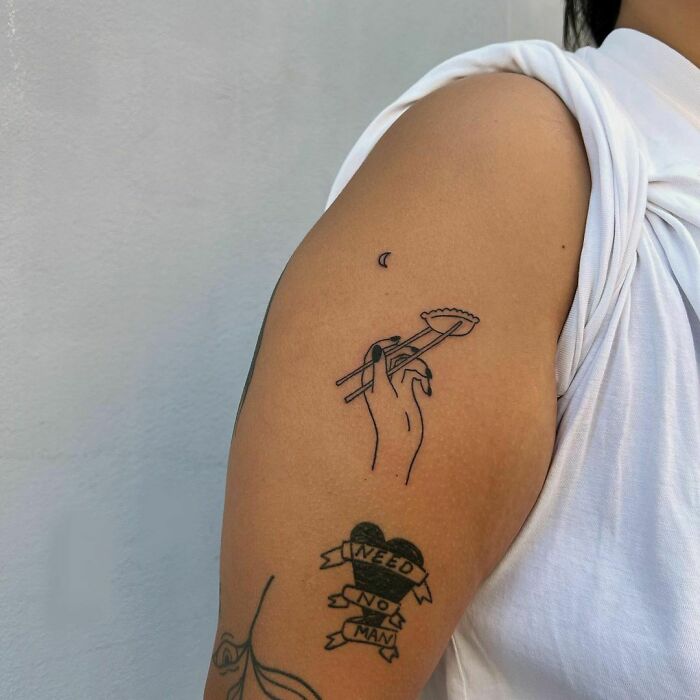 Food tattoo of a hand holding a dumpling with chopsticks on an arm.
