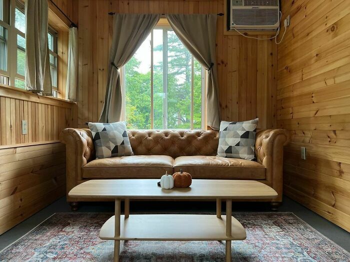 Brown leather couch with grey pillows in cozy wood-paneled living room of tiny house design interior.