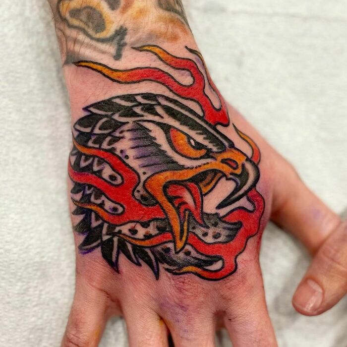 American traditional tattoo of an eagle head with fiery accents on a person's hand.