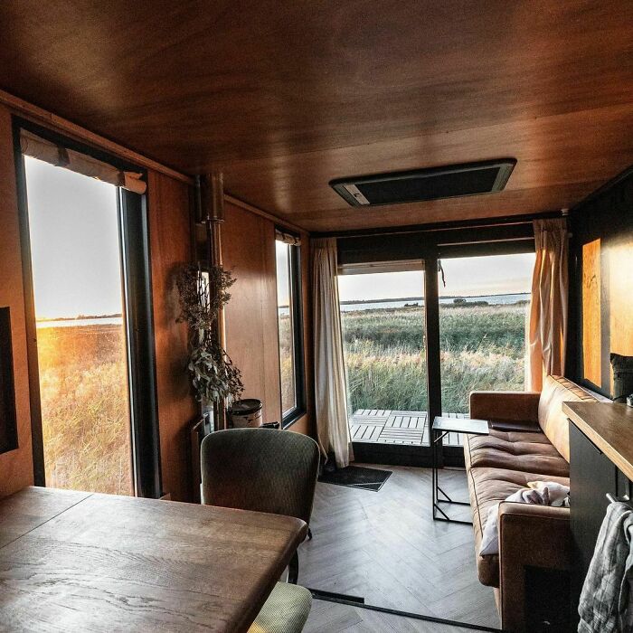 Cozy brown tiny house interior with wide windows showcasing natural light and outdoor views in a compact living space.