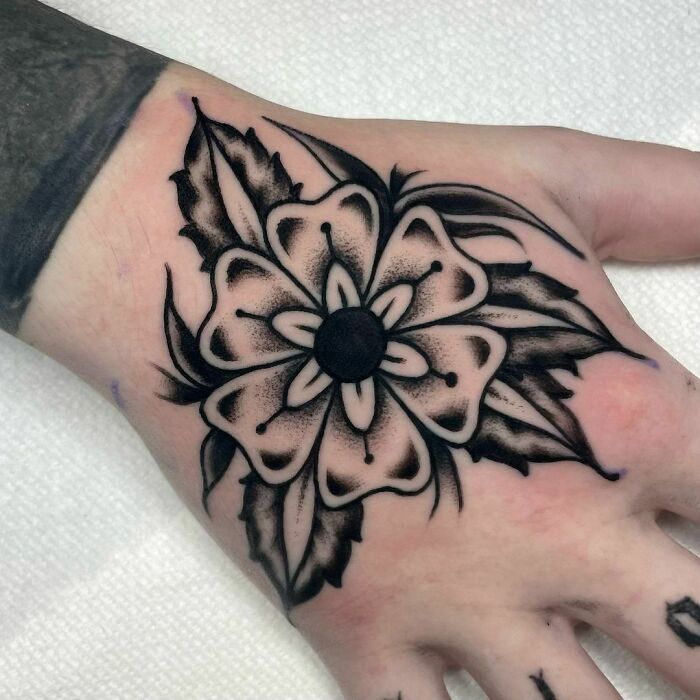 American traditional tattoo of a black and white flower on a hand, showcasing classic design elements.