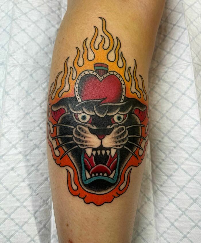 American traditional tattoo of a roaring panther with flames and a heart crown, on a person's leg.
