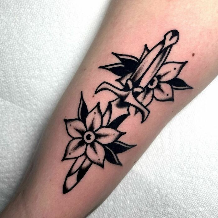 American traditional tattoo of a dagger and flowers on forearm.