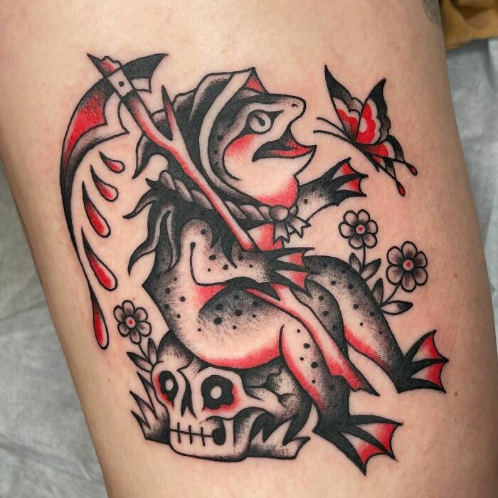 American traditional tattoo featuring a frog on a skull, holding a scythe with blood droplets and facing a butterfly.