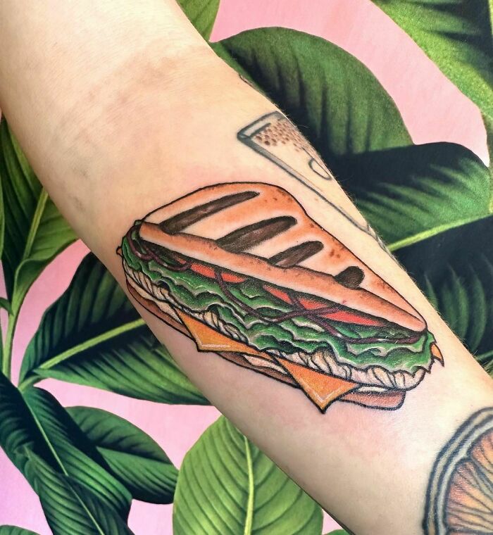 Watercolor food tattoo of a sandwich on an arm, showcasing vibrant colors and artistic detail.