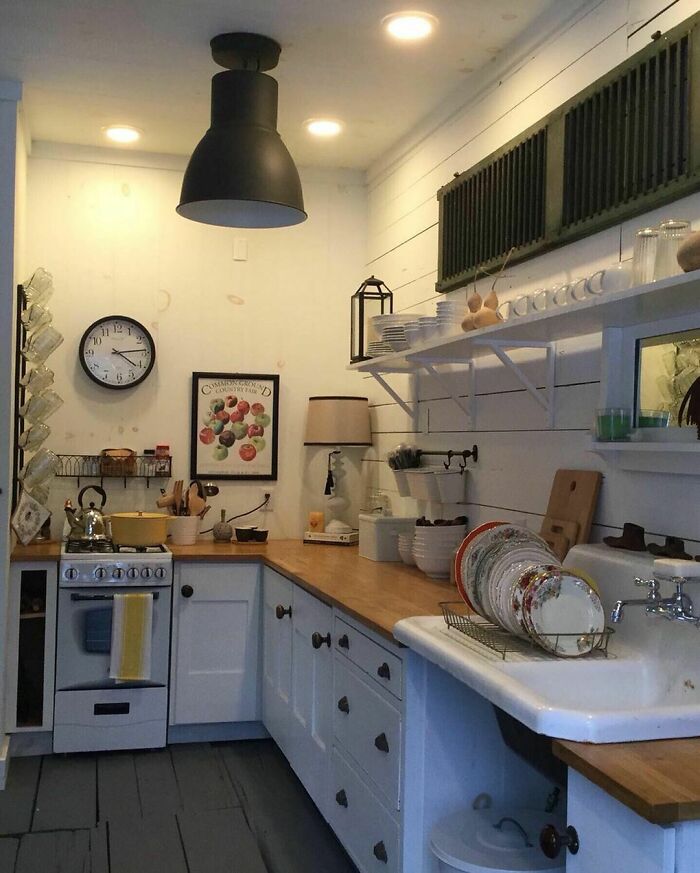 Cozy tiny house kitchen with white cabinets, wooden countertops, and open shelving, showcasing charming compact design.