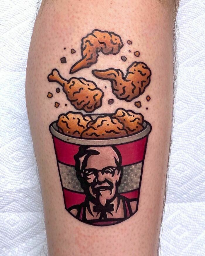 Watercolor tattoo of KFC chicken bucket with flying drumsticks, illustrating a creative food ink-spiration design.