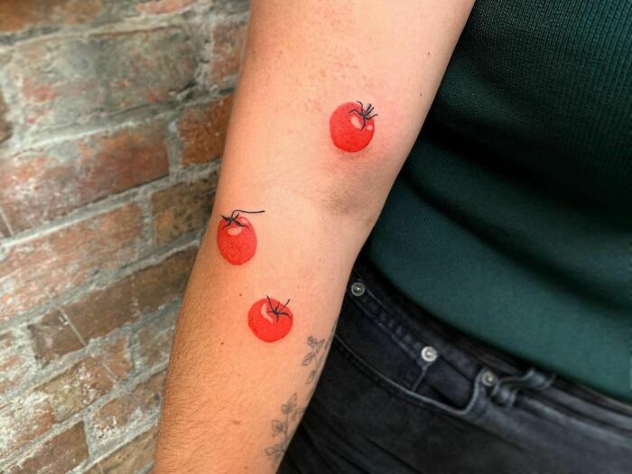 Watercolor tattoo of three tomatoes on an arm, showcasing creative food ink-spiration.