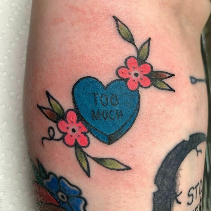 American traditional tattoo with a blue heart labeled "Too Much" and red flowers.