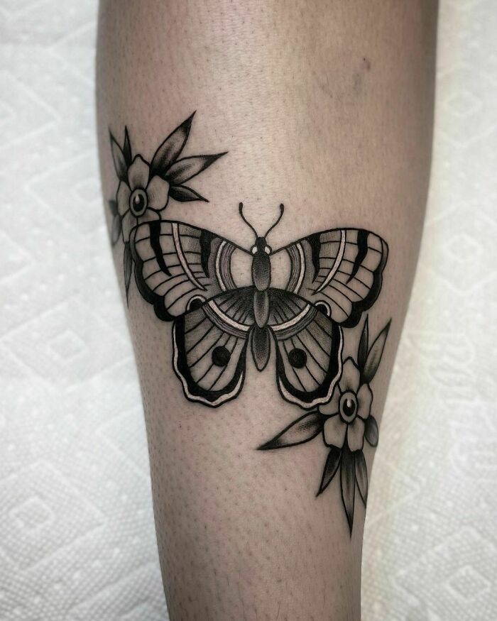 American traditional butterfly tattoo with flowers on a leg.