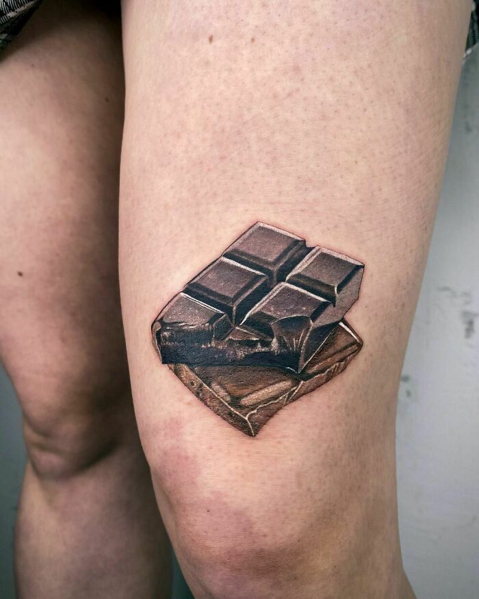 Watercolor tattoo of dark chocolate on a person's thigh, showcasing a creative food-inspired design.