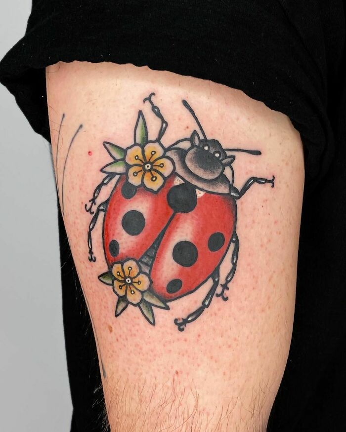 American traditional tattoo of a ladybug with flowers on an arm.
