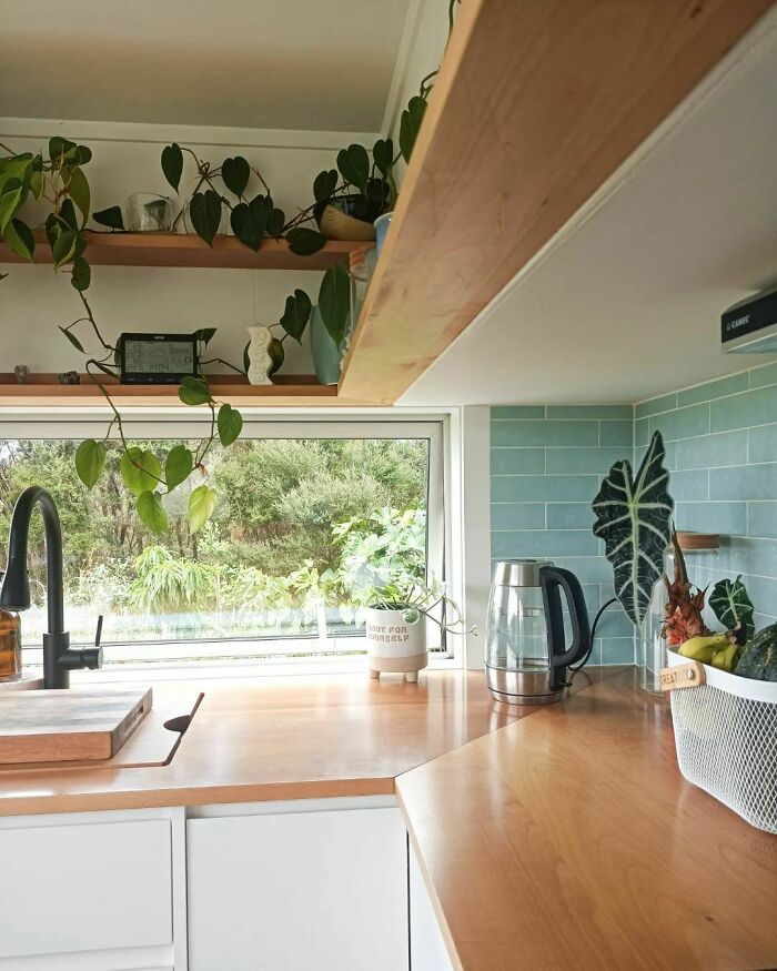 White kitchen cabinets with wooden countertops and plants in a bright tiny house design kitchen space.