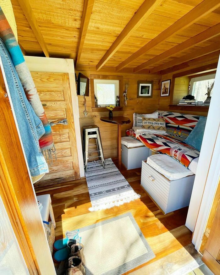 Cozy interior of a tiny house with wooden walls, vibrant textiles, and a small dining area under natural light.