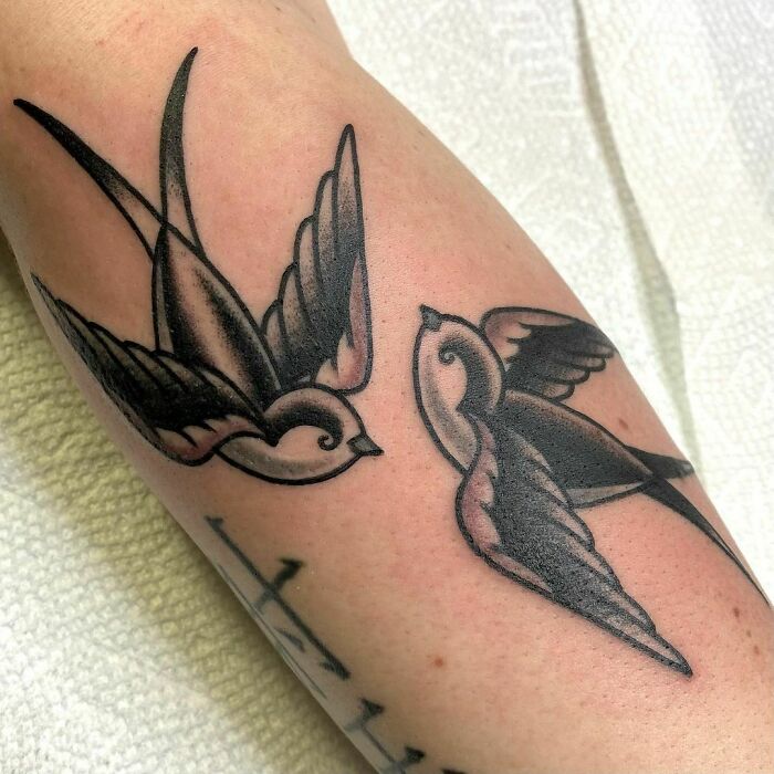 Two American traditional tattoos of swallows on an arm, showcasing bold black ink designs.