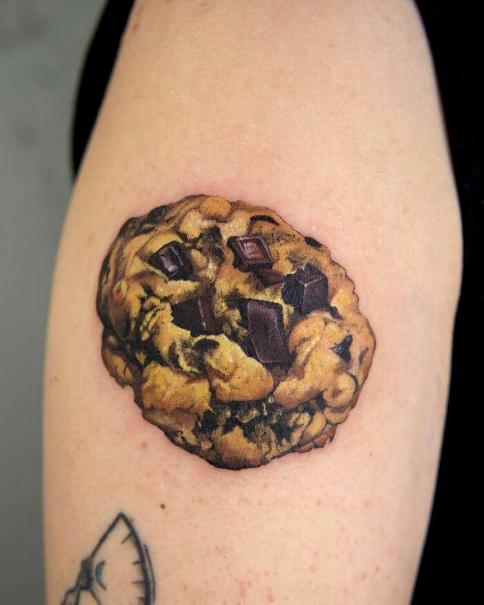Watercolor cookie tattoo on arm featuring chocolate chips.