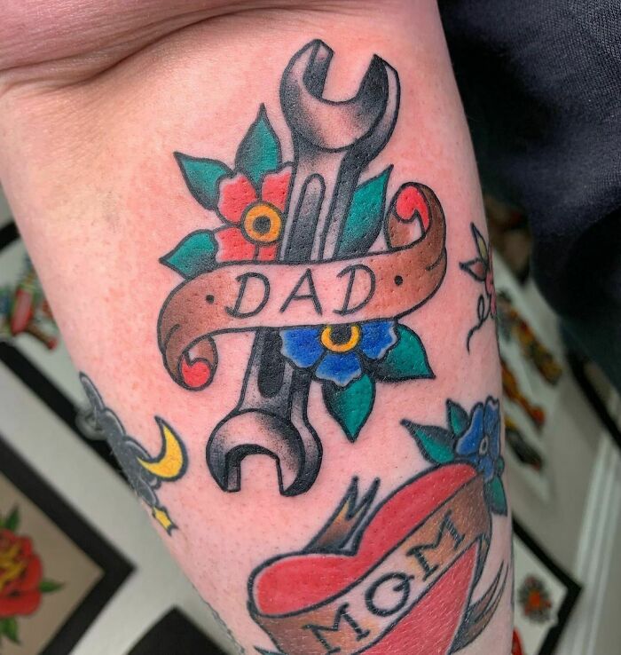 American traditional tattoo of a wrench with "Dad" banner and flowers, creating a bold statement piece.