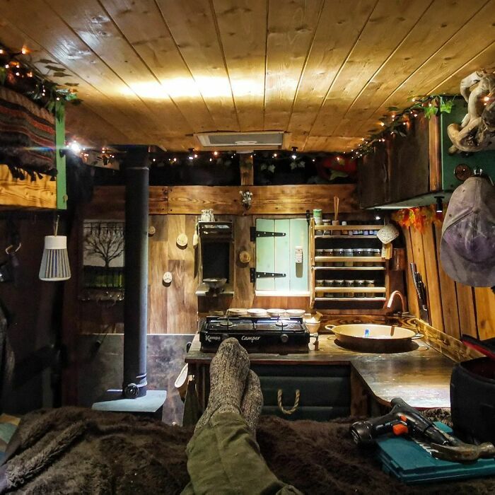 Cozy tiny house interior with wooden walls, ceiling, and compact kitchen space featuring a stove and rustic decor.