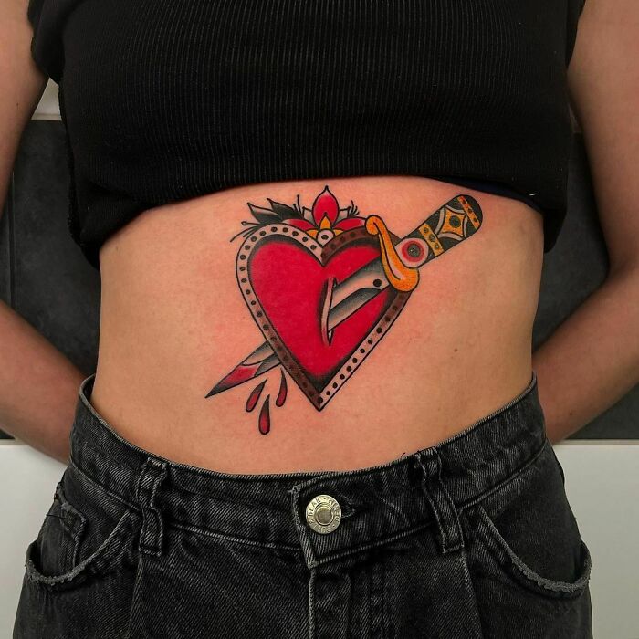 American traditional tattoo of a dagger through a heart on a person's torso, showcasing bold colors and classic design.