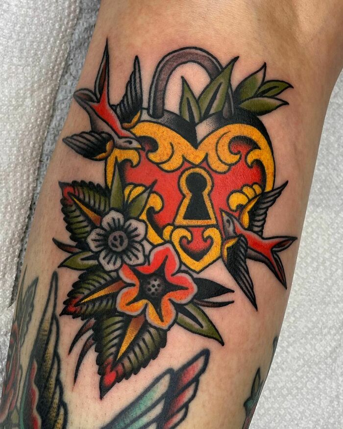 Colorful American traditional tattoo featuring a heart-shaped lock with birds and floral elements.