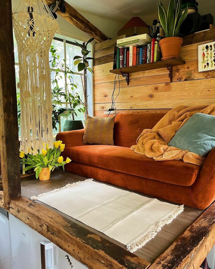 Cozy tiny house interior with a warm orange sofa, macramé decor, and bright yellow tulips, embodying stylish design.