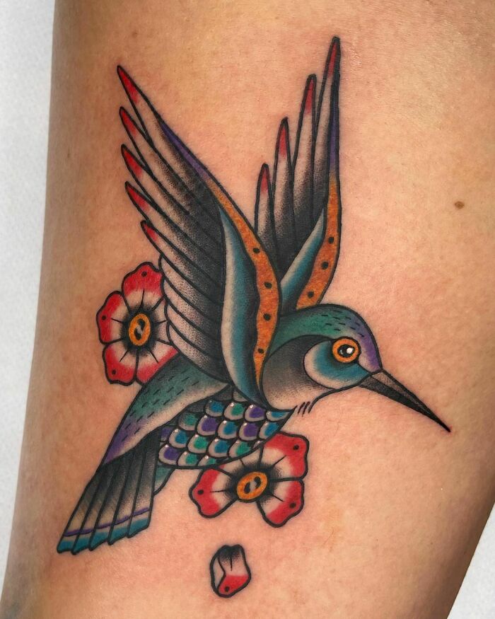 American traditional tattoo of a colorful hummingbird with flowers on skin.