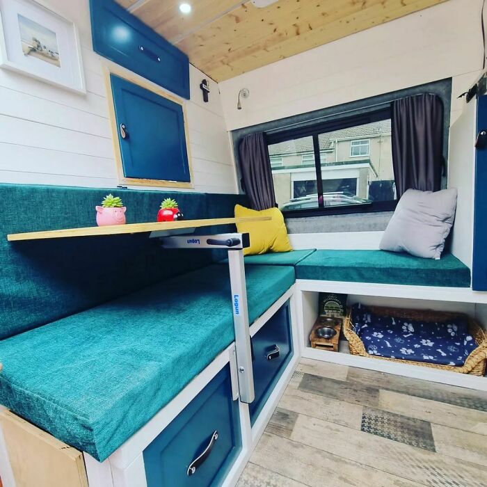 Compact, cozy interior of a tiny house featuring teal cushions, a folding table, and ample storage space.