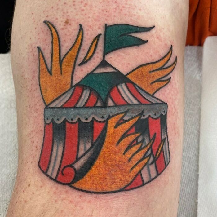 American traditional tattoo of a circus tent with flames and a flag, featuring bold colors and classic design elements.