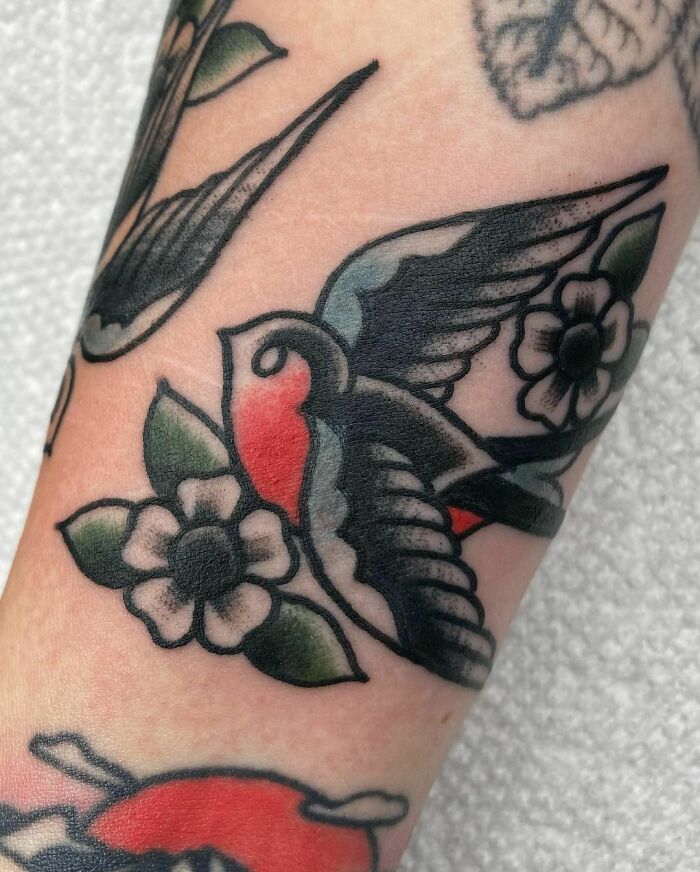 American traditional tattoo of a colorful swallow surrounded by flowers.