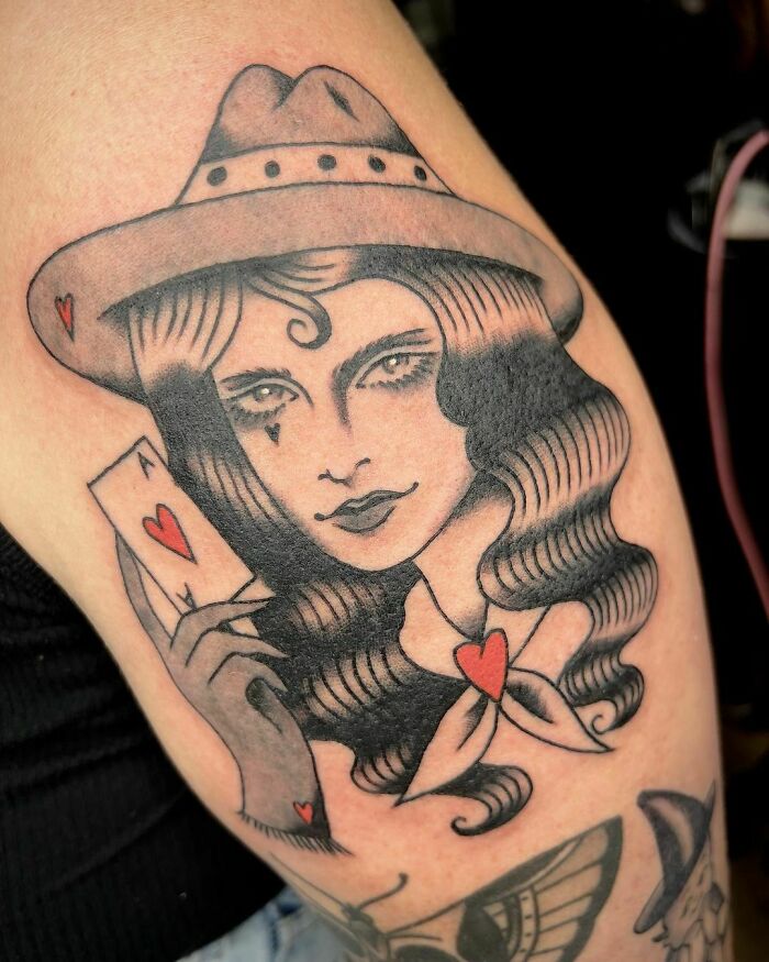 American traditional tattoo of a woman with wavy hair holding playing cards, featuring classic black and red details.